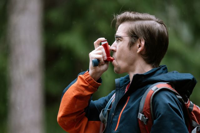 young man hiking in woods using an asthma inhaler