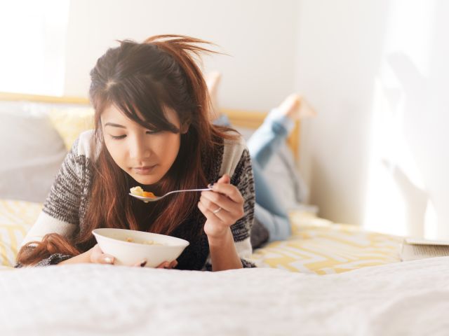 a young Asian woman enjoys a bowl of chicken soup while in bed