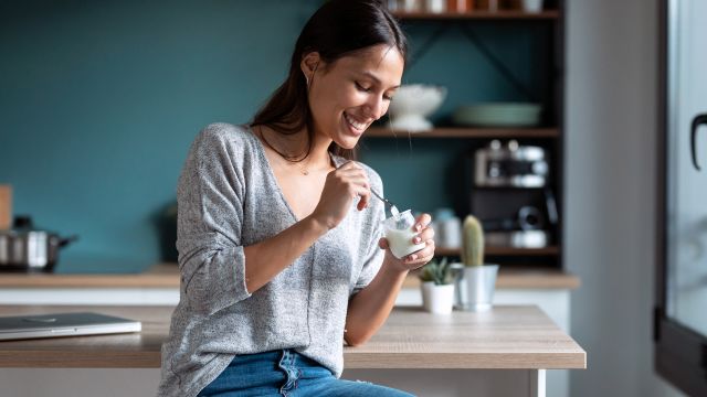 smiling woman eating a small cup of yogurt