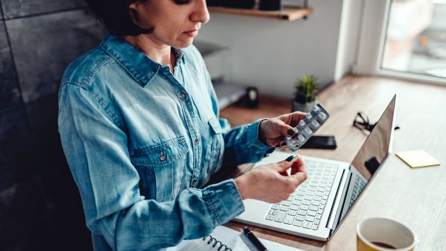 Woman at desk taking a pill from a blister pack