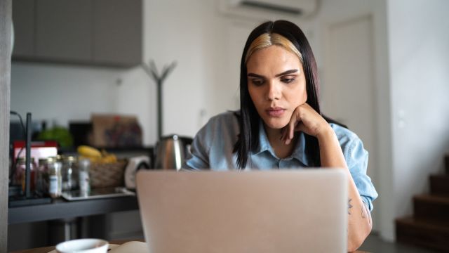 Transgender woman using a laptop at the kitchen table.