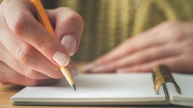 A woman writes in her journal with a pencil.