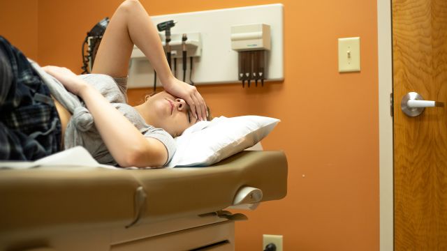 A young woman experiences abdominal pain while waiting in an exam room to see her healthcare provider.