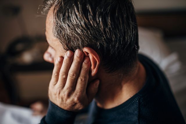 a middle aged man sitting alone places his hand against his year