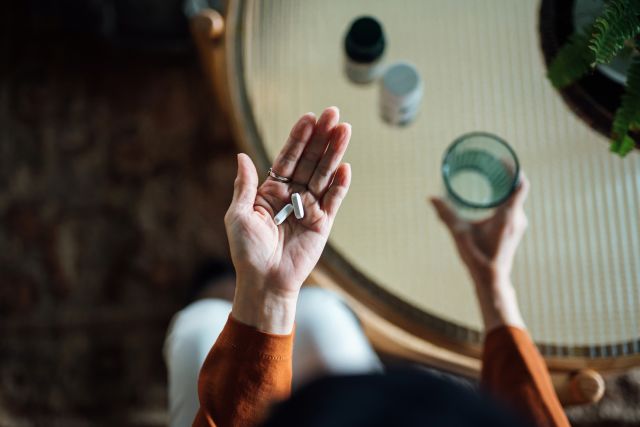 hands holding two pills and a glass of water