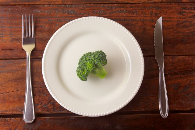 piece of raw broccoli on a plate with fork and knife alongside