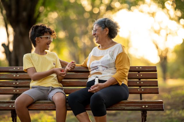 a young boy and his grandmother sit on a park bench laughing and talking