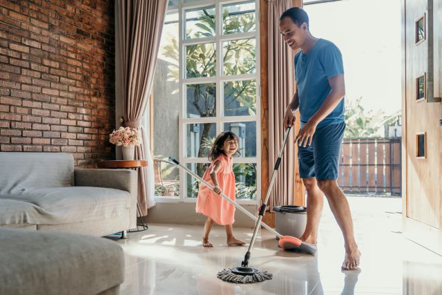 a young man and his young daughter enjoy getting exercise while sweeping the floors of their home 