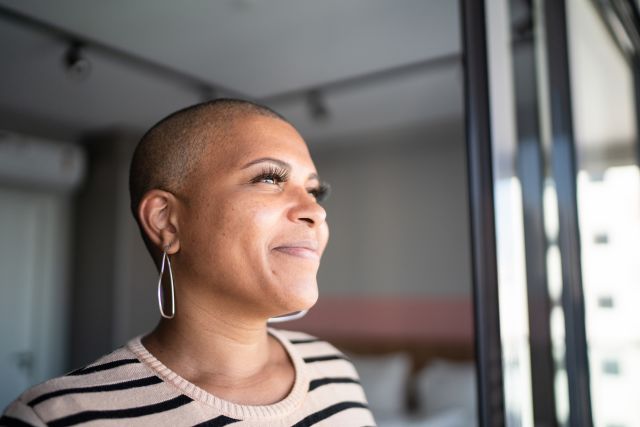 a confident, smiling Black woman breast cancer survivor looks out into the distance