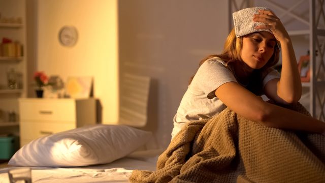 A woman has a cold cloth on her head to ease headache pain.