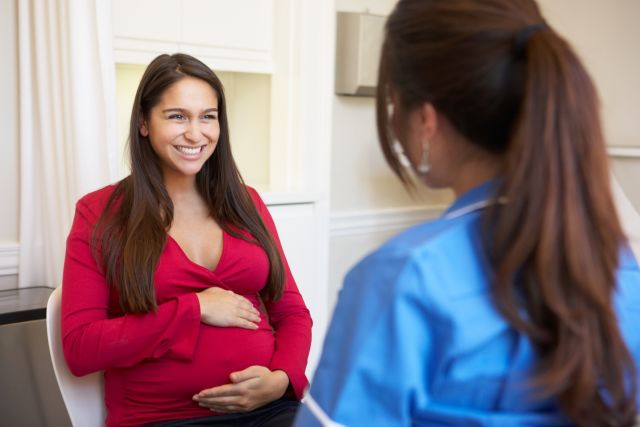 a smiling pregnant woman touching her belly speaks with a nurse about pregnancy concerns