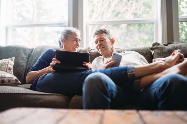 A happy middle aged White couple relaxes on a couch, looking at a computer screen