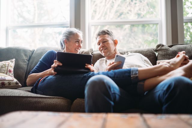 A happy middle aged White couple relaxes on a couch, looking at a computer screen