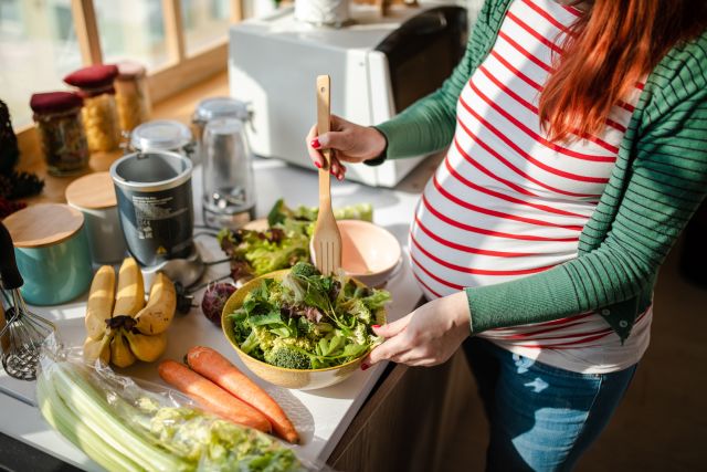 a pregnant person, seen from the neck down, prepares a healthy salad 