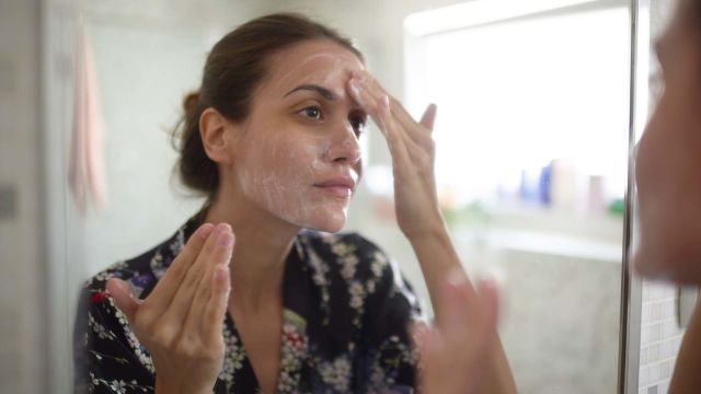Woman applies acne medication to face.