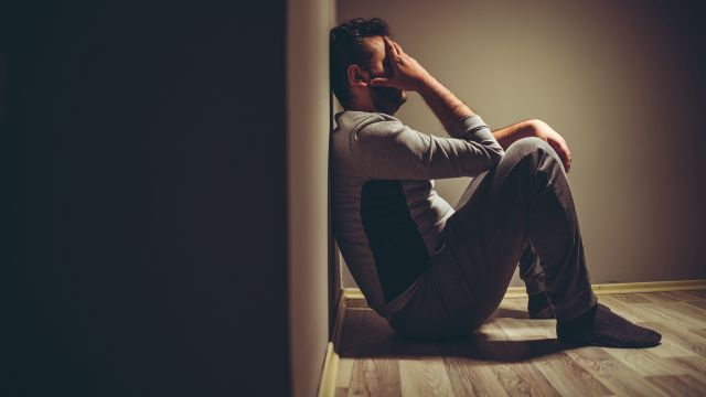 A man sits alone in a dark room. Many people with HIV struggle with the mental burden of living with a chronic illness.