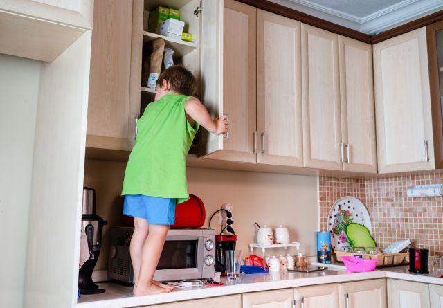 Young child peers into kitchen cabinet from countertop