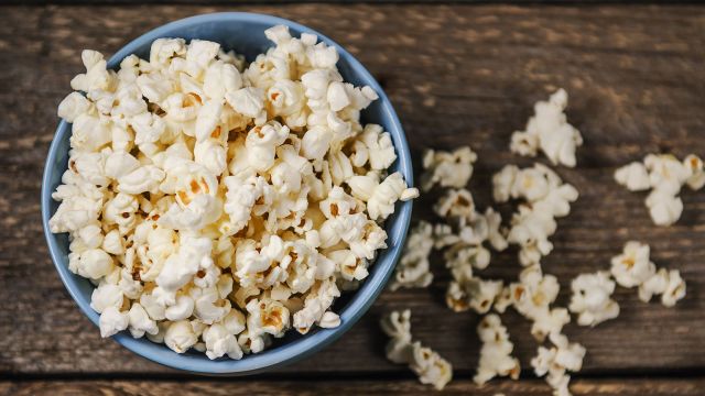 Popcorn in bowl with some kernels spread out on table.