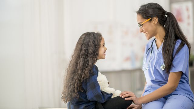 A pediatrician talks to a smiling young girl.