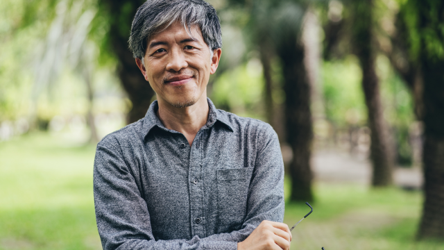 Middle-aged Asian man smiling outdoors.