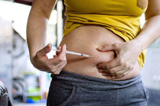 Photo of person pulling up yellow tshirt and injecting fertility medication on the right side of the abdomen