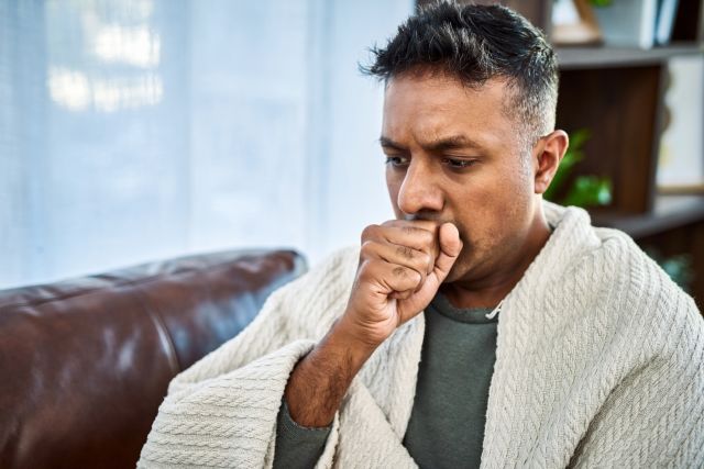 a South Asian man experiencing congestion coughs into his hand