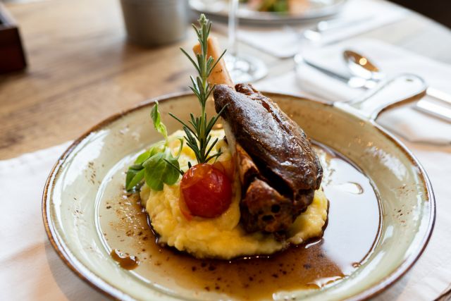 closeup of a gourmet plate of braised lamb shank over mashed potatoes, garnished with rosemary