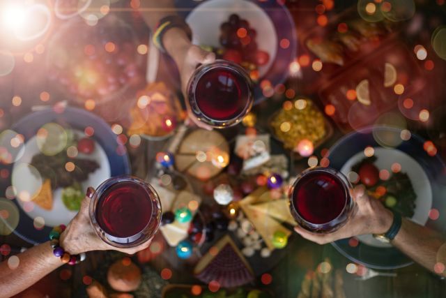 hands toasting wine over holiday party food buffet
