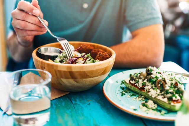 View of a man eating fresh vegan salad with chickpeas balls and sesame sauce on rustic wooden table