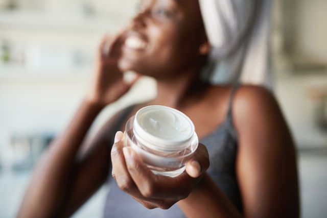 closeup of a tub of skin cream that a woman is applying to her face after a shower