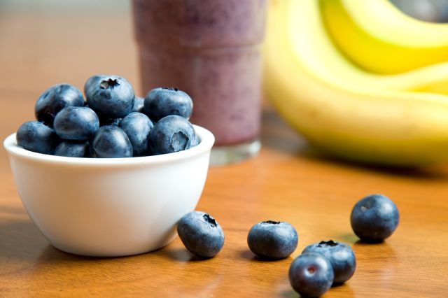 a bowl of fresh blueberries in front of bananas and a smoothie