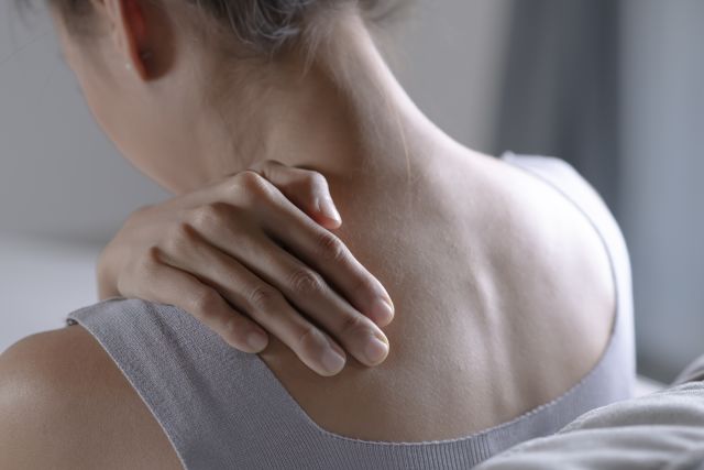 Rear view closeup of a woman rubbing the back of her shoulder from stiffness caused by fibromyalgia