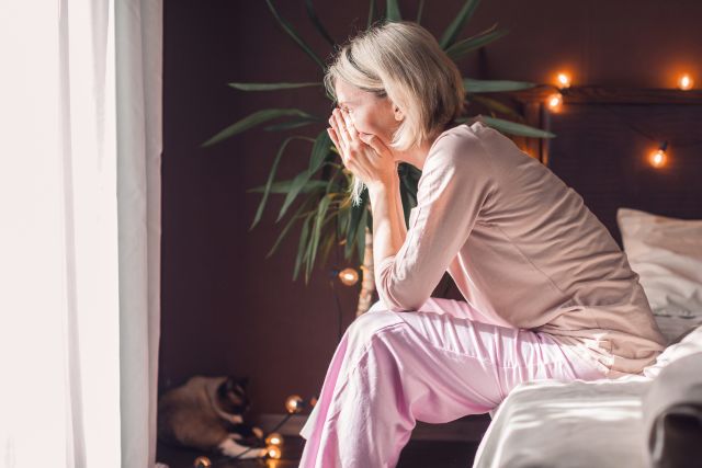 depressed woman with head in hands sitting on edge of bed