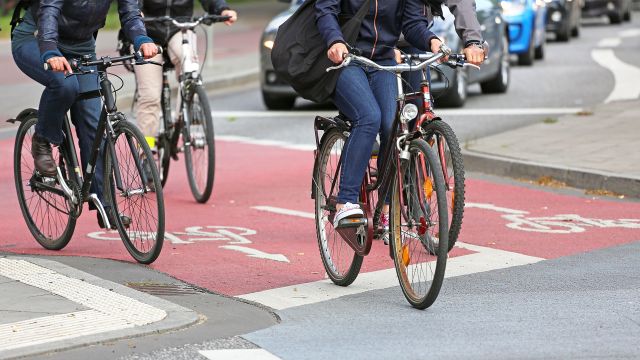 three cyclists wearing commuter clothing are biking in red bike lanes