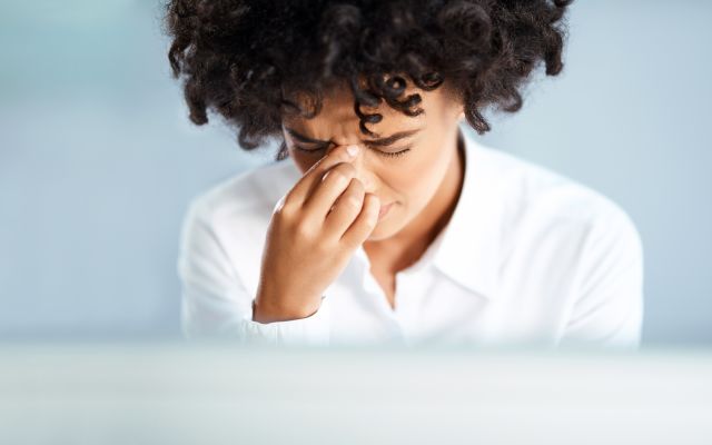 A woman experiences sinus congestion while at work in an office. Nasal polyps can block airways and contribute to congestion, infections, and other symptoms.