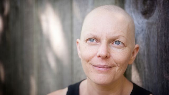 A woman battling cancer smiles while looking into the distance.