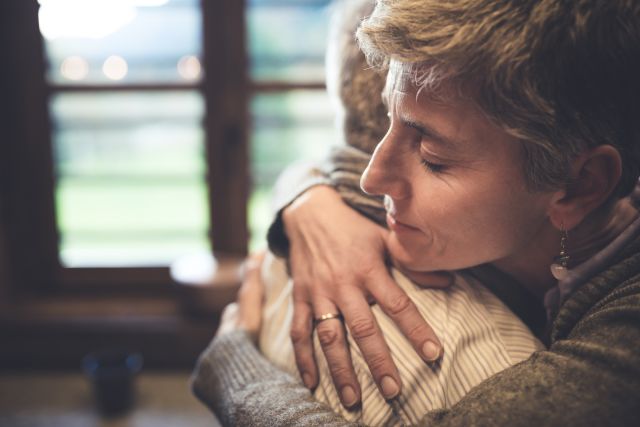 A middle aged white woman with short brown hair hugs her elderly father