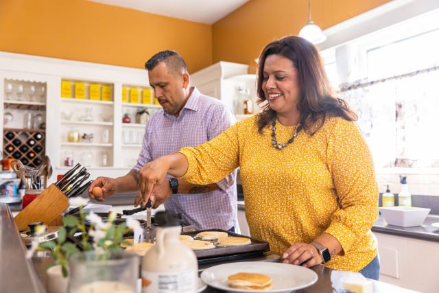 a middle-aged Latino couple cooks a meal of pancakes in their kitchen 
