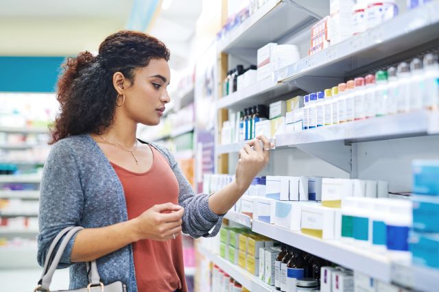 A young Latina woman reads the labels on beauty products in the pharmacy to select a healthy product.