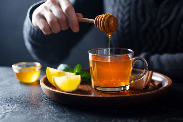 person dropping honey into lemon tea