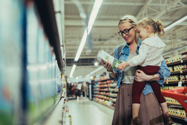A mother and a small child read a food label together in a supermarket, checking ingredients for any food allergens.