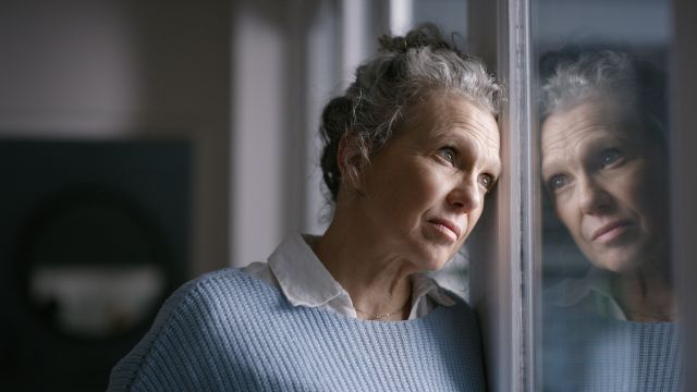 An older woman looks out a window while dealing with symptoms of depression.