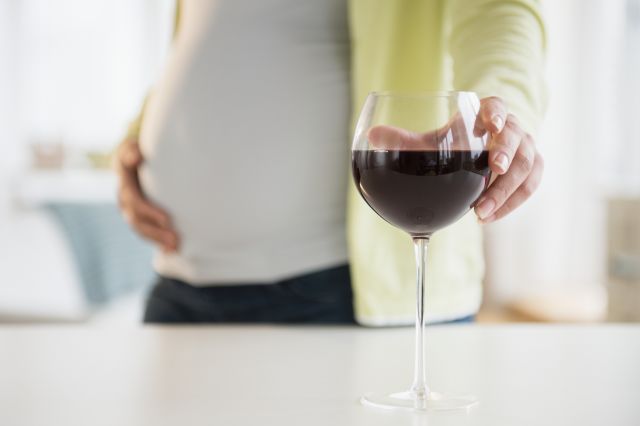 pregnant person reaching for a glass of red wine