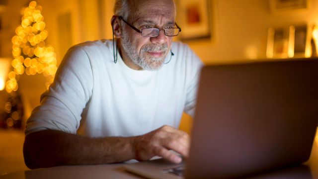 A senior man prepares for an upcoming healthcare appointment by putting together a list of questions using a laptop computer.