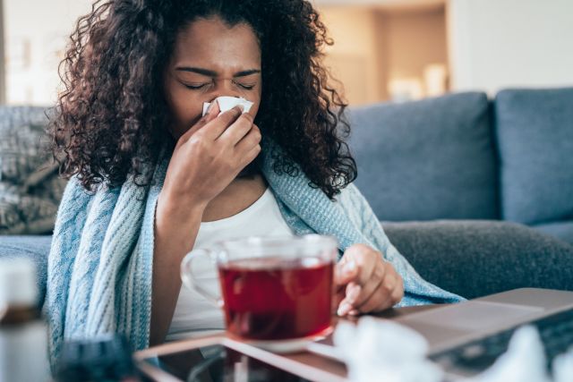 sick woman on couch blowing nose and drinking tea