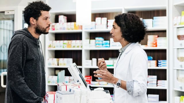 A man in his 30s speaks with a pharmacist while picking up a new prescription medication for food allergies.
