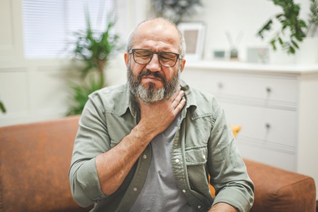 a middle aged white man winces and grabs his throat as he experiences the burning sensation of acid reflux