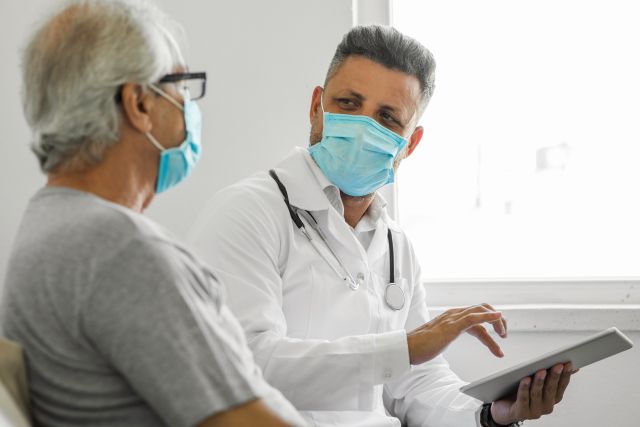 an older adult man consults with a middle aged male doctor about an illness caused by COVID-19