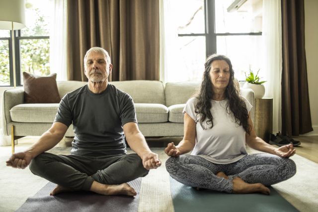 a middle aged white man and woman sit side by side in meditation pose, using meditation to help relieve pain