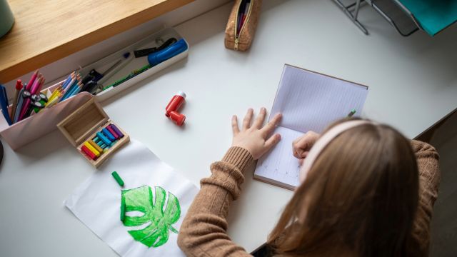 A young girl does homework at a desk with an asthma inhaler close by. Asthma is a lifelong health condition, and school is an opportunity for a child to take steps toward managing asthma on their own. 